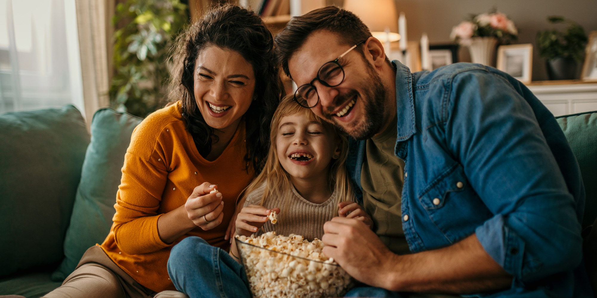 Family watching a funny movie on the couch in their home and eating popcorn