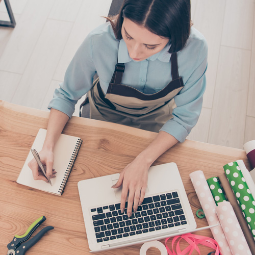 A woman on her computer and writing on paper. Looking like she is multitasking and getting organized.